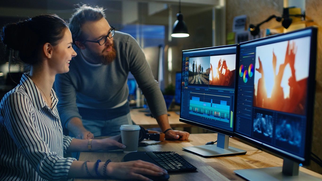 photo of two people looking at a video editing project on a computer screen monitor